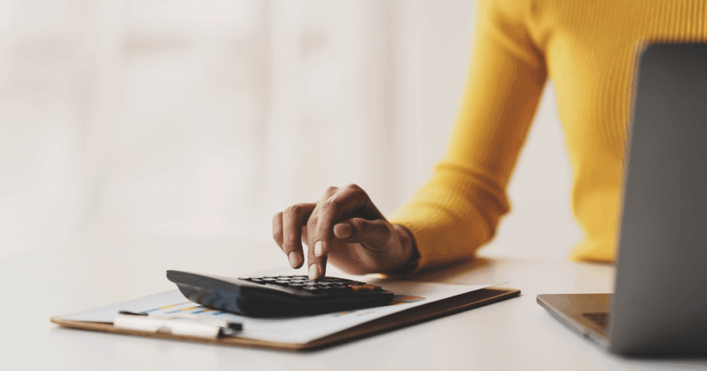 Pessoa analisando relatórios e utilizando calculadora sobre uma mesa, representando o controle e elaboração de demonstrações financeiras.