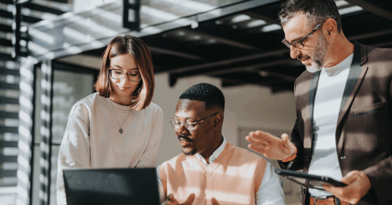 Equipe de profissionais reunida em escritório analisando informações no notebook e tablet, discutindo estratégias e tomada de decisão para fortalecer a competitividade da empresa.