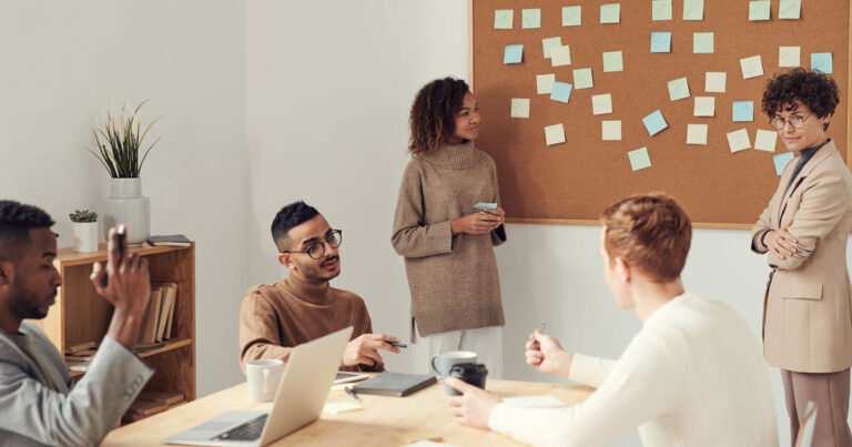 Profissionais reunidos em uma sala de reuniões analisando um quadro com anotações, enquanto discutem estratégias e políticas de recursos humanos