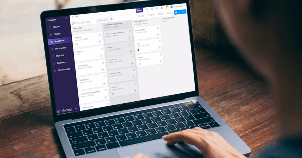 Pessoa usando um laptop exibindo um sistema CRM com interface de gerenciamento de projetos, com colunas de tarefas e etapas visíveis na tela.