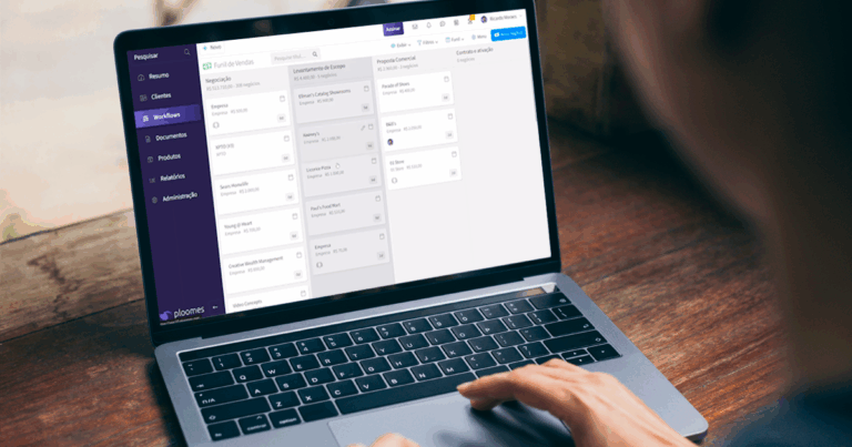 Pessoa usando um laptop exibindo um sistema CRM com interface de gerenciamento de projetos, com colunas de tarefas e etapas visíveis na tela.