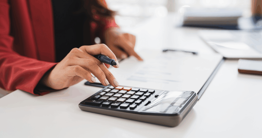 Pessoa calculando valores em uma calculadora sobre uma mesa, representando o cálculo e a análise do CMV (Custo da Mercadoria Vendida).