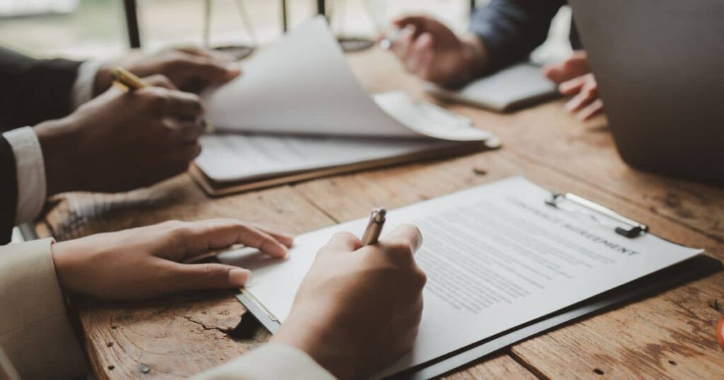 Profissionais analisando e assinando documentos sobre uma mesa, representando a rotina e responsabilidades de um gestor de contratos.