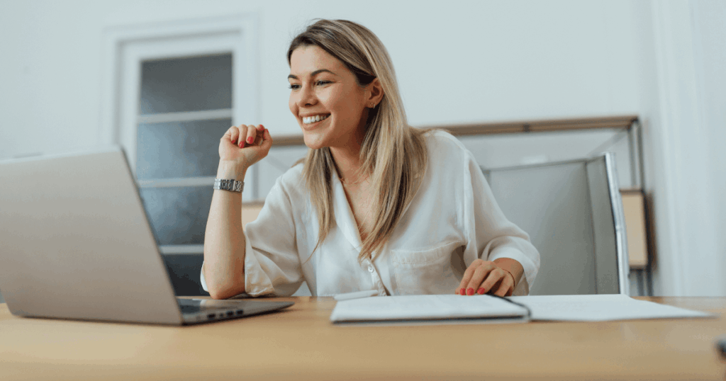 Mulher sorrindo enquanto analisa informações no notebook em um escritório, representando um momento de tomada de decisão nas empresas
