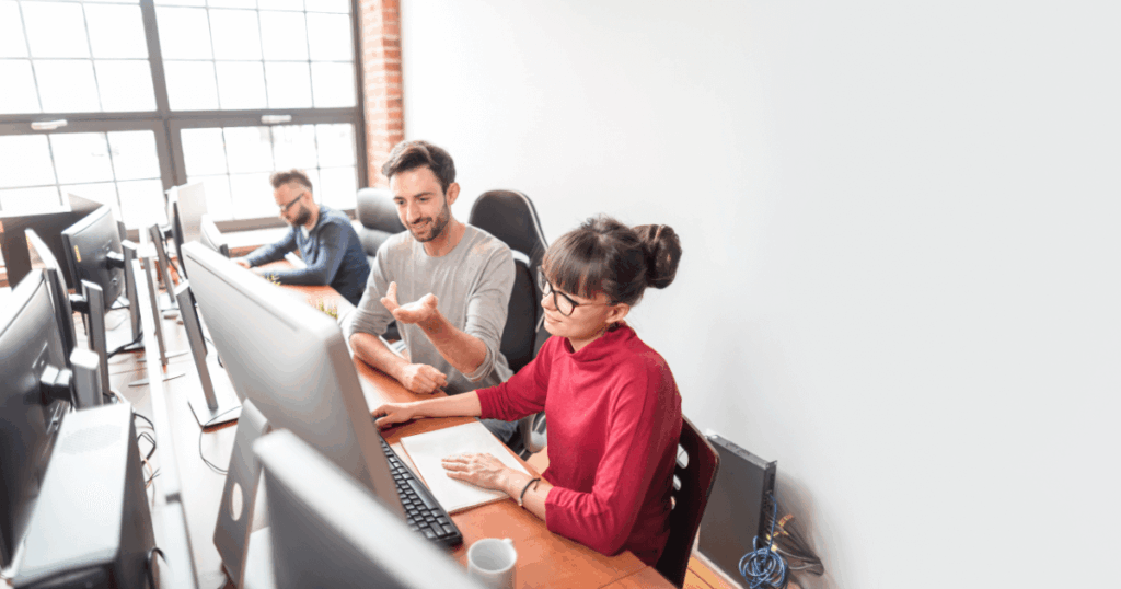 Equipe de profissionais trabalhando em computadores em um escritório moderno, colaborando e discutindo processos, ilustrando serviços de BPO (Business Process Outsourcing).