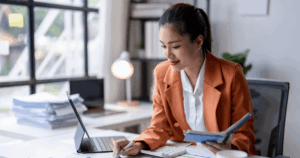 Profissional mulher de negócios analisando documentos e utilizando calculadora no escritório, representando o cálculo do ponto de equilíbrio financeiro de uma empresa.