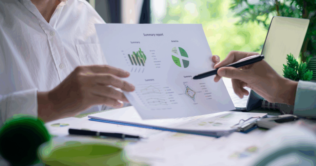 Duas pessoas analisando gráficos e relatórios impressos sobre desempenho e sustentabilidade em um ambiente de trabalho, representando o conceito de análise ambiental.