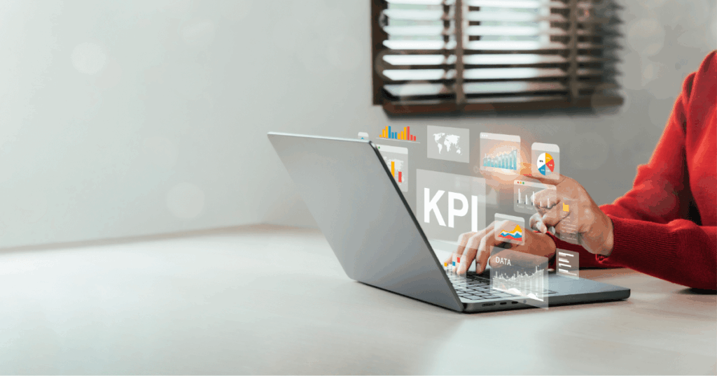 Pessoa trabalhando em laptop com gráficos digitais e painéis de KPI projetados na tela, representando análise de dados e métricas.
