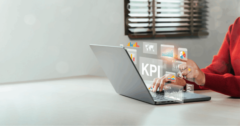Pessoa trabalhando em laptop com gráficos digitais e painéis de KPI projetados na tela, representando análise de dados e métricas.