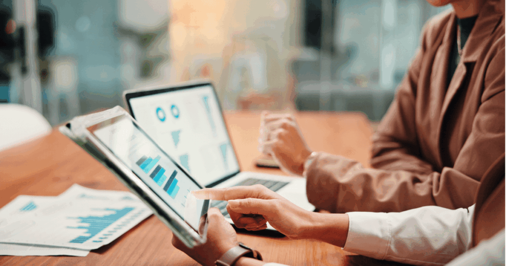 Profissionais analisando gráficos financeiros em tablet e notebook, representando o cálculo e a gestão do IRRF nas empresas.