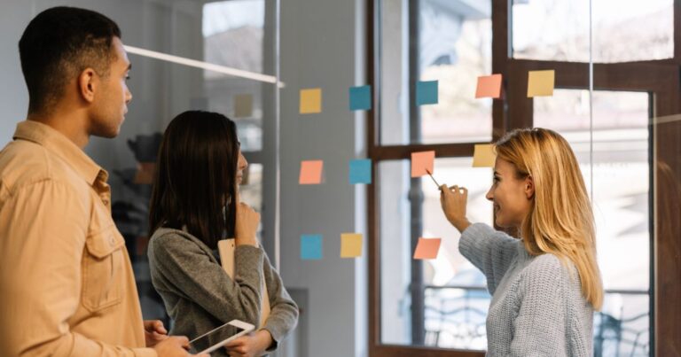Equipe colaborando em reunião de planejamento com post-its coloridos em vidro, típica de metodologia ágil Scrum em ambiente corporativo.