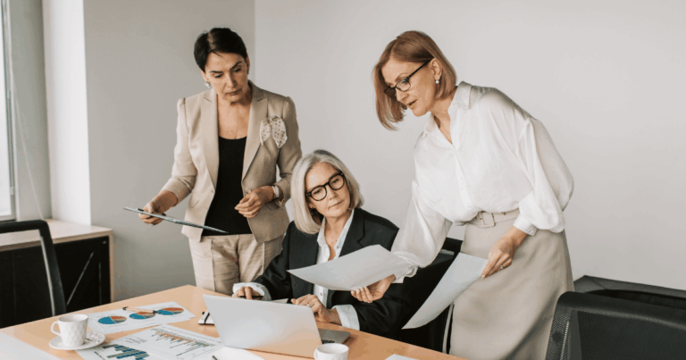 Mulheres executivas em reunião analisando relatórios e discutindo melhorias na cultura organizacional.