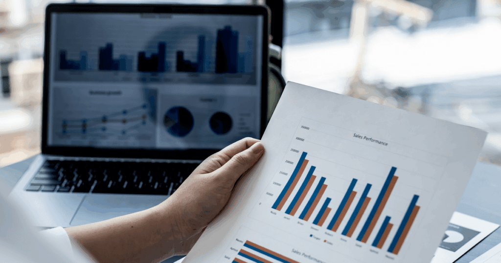 Análise de gráficos de desempenho de vendas em papel e no notebook, representando estratégias de comissionamento baseadas em metas e performance comercial