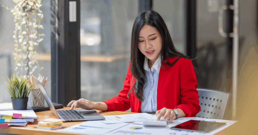 Mulher analisando relatórios financeiros e gráficos em um ambiente de escritório moderno, representando a conferência e organização de dados para elaboração de um balancete.