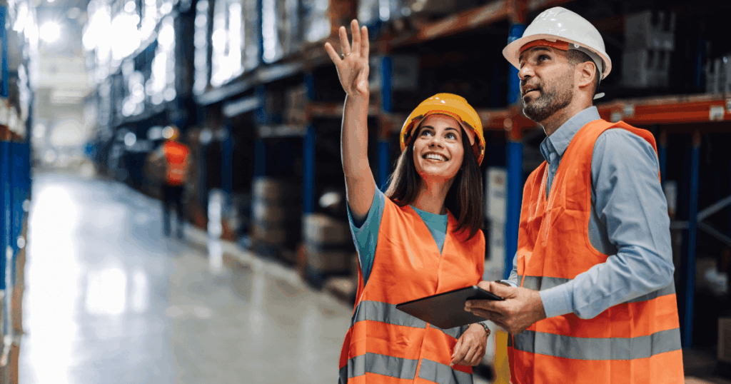 Profissionais com coletes e capacetes analisando operações em centro de distribuição, representando o uso de ERP logística para otimizar processos e gestão de estoque.