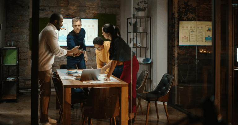 Equipe diversa de profissionais colaborando em uma sala de reunião moderna, analisando dados em um notebook e gráficos na parede, representando o ambiente dinâmico e colaborativo típico de uma lean startup.