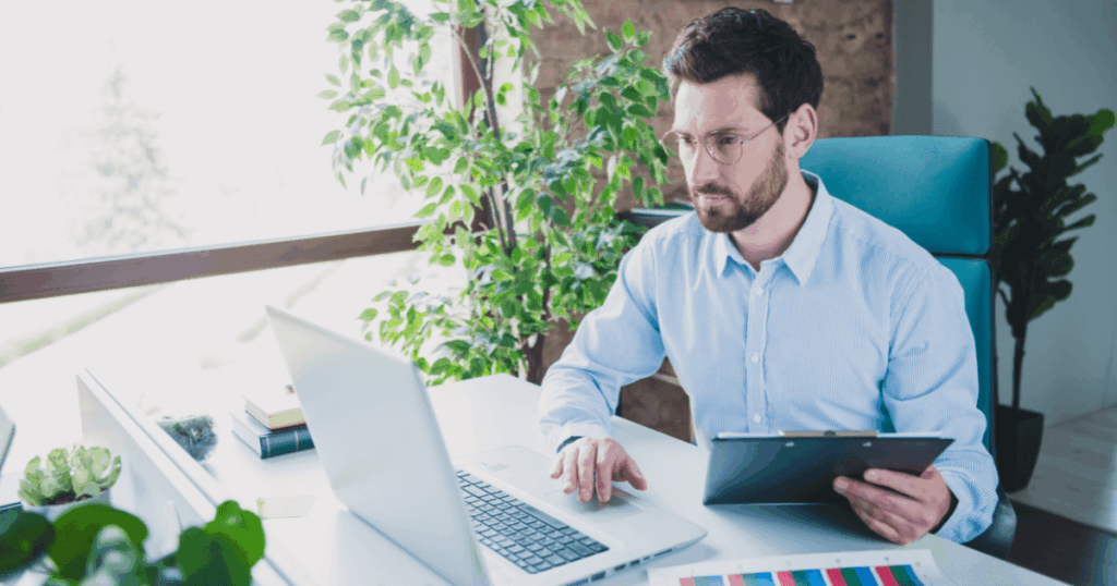 Executivo analisando gráficos de desempenho financeiro e ROA (Retorno sobre Ativos) em ambiente corporativo, utilizando notebook e tablet em escritório moderno com luz natural.