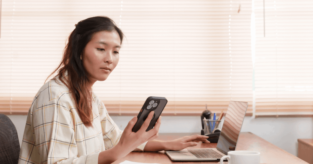 Mulher em ambiente de escritório utilizando o celular e o notebook para acompanhar informações financeiras relacionadas ao DDA.