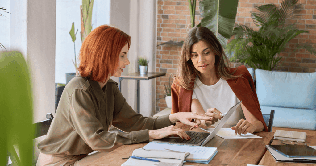 Duas mulheres analisando dados em um notebook em ambiente corporativo, ilustrando a aplicação do Princípio de Pareto para identificar os 20% de ações que geram 80% dos resultados.