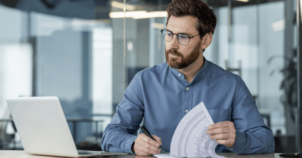 Profissional analisando documentos fiscais e tributários em frente ao computador, representando o cumprimento das obrigações acessórias no ambiente corporativo.