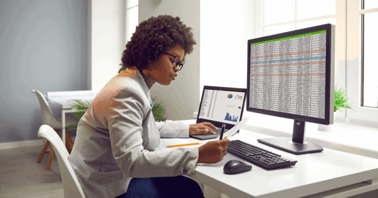 Profissional analisando dados financeiros em planilhas no computador, com foco em controle financeiro empresarial, acompanhado de gráficos e números em monitores duplos, em um ambiente de escritório moderno e bem iluminado.