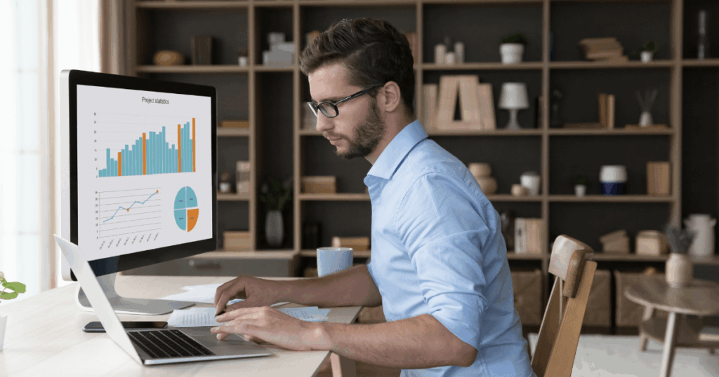 Profissional analisando indicadores financeiros em gráficos de barras, linhas e pizza na tela do computador em ambiente de escritório moderno.