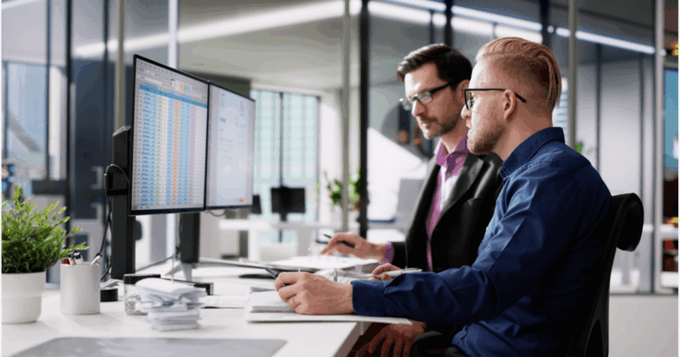 Profissionais avaliando planilhas em dois monitores durante uma análise de rentabilidade no setor financeiro de uma empresa.