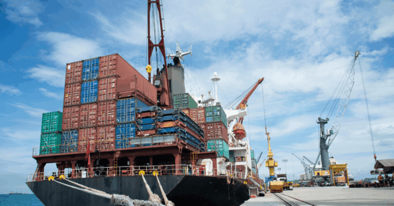 Navio cargueiro carregado com contêineres em porto comercial, representando os impactos das disputas e barreiras econômicas de uma guerra tarifária no comércio internacional.