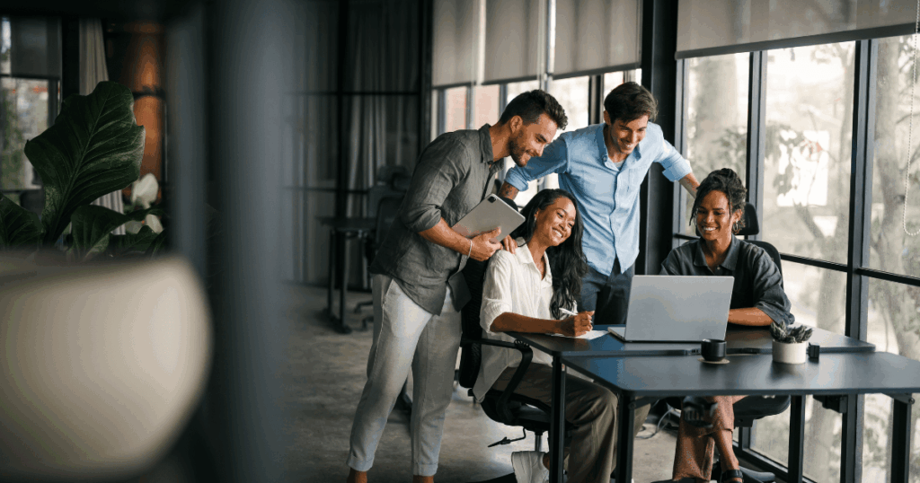 Equipe reunida em um escritório moderno, sorrindo enquanto analisa dados em um notebook, representando o uso colaborativo de um software de RH.