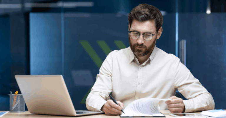 Homem analisando documentos financeiros em um escritório moderno, com notebook aberto sobre a mesa, representando a aplicação das normas do IFRS 16 na gestão contábil.
