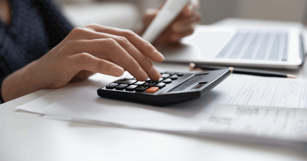 Pessoa utilizando calculadora e analisando documentos financeiros ao lado de um notebook, representando o uso da IA para apoiar empresas na adaptação à reforma tributária.