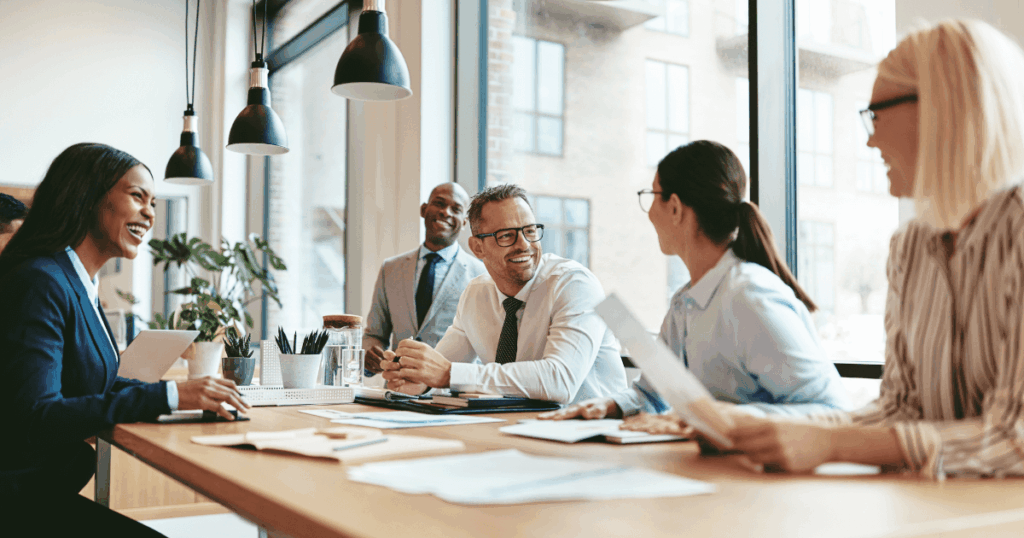 Equipe de profissionais reunida em uma sala de reunião, sorrindo e interagindo de forma colaborativa, representando práticas de DHO focadas em desenvolvimento humano e organizacional.