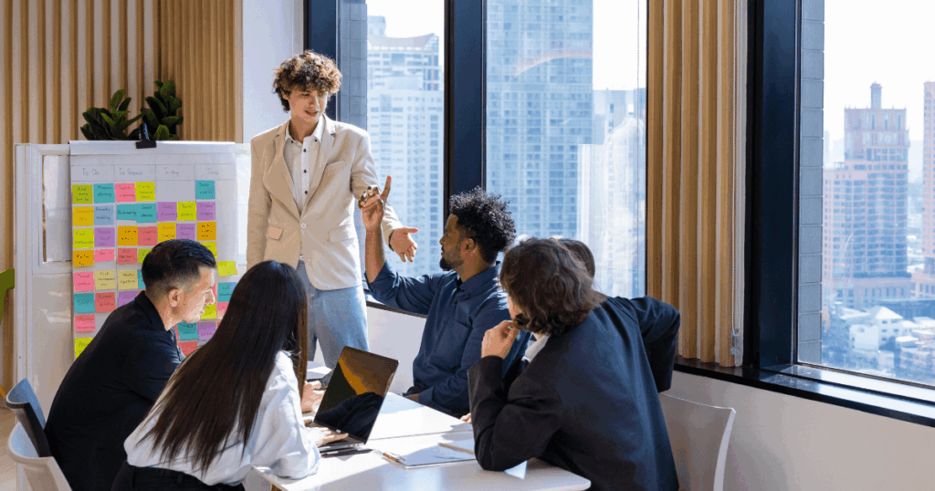 Reunião de equipe em um escritório moderno, com um líder apresentando ideias a um grupo de colaboradores ao redor de uma mesa, ilustrando práticas de gestão estratégica de pessoas.