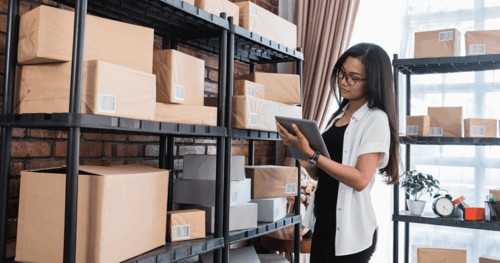 Profissional utilizando tablet para conferir estoque em prateleiras com caixas, representando a previsão de demandas e o controle de inventário.