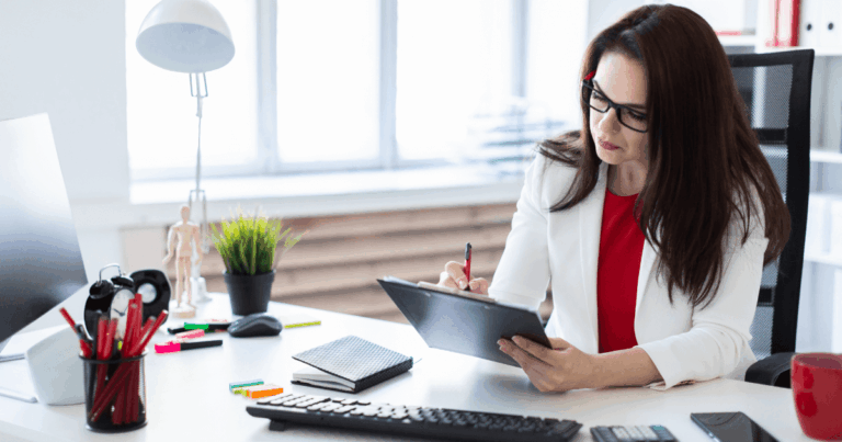 Profissional trabalhando em escritório, anotando informações financeiras em uma prancheta sobre a mesa, representando atividades de tesouraria e gestão financeira.
