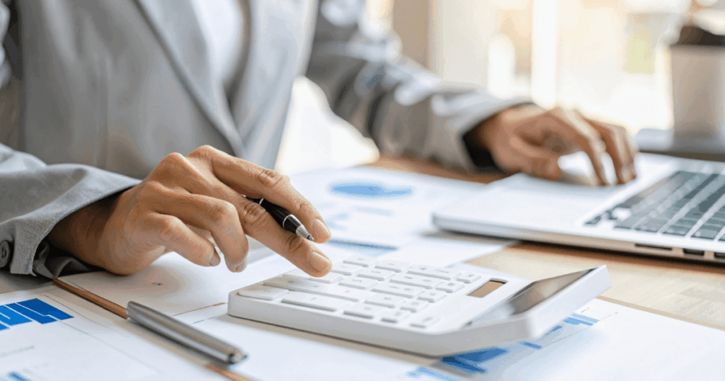 Profissional realizando cálculos financeiros com calculadora, documentos e notebook sobre a mesa, representando a apuração de impostos e o controle fiscal relacionado ao ISS nas rotinas contábeis e tributárias.