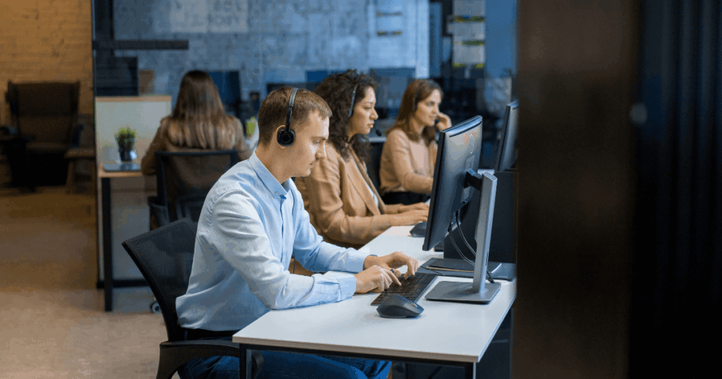 Pós-vendas em ambiente corporativo, com equipe de atendimento trabalhando em computadores e headsets para suporte e relacionamento com clientes.