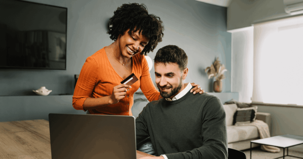 Casal realizando uma compra online em notebook, com uso de cartão de crédito em ambiente doméstico, representando a experiência de consumo no varejo digital e a integração entre tecnologia, conveniência e decisão de compra.
