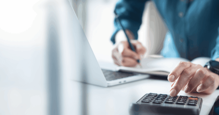 Pessoa utilizando uma calculadora enquanto faz anotações ao lado de um notebook, representando o cálculo e a organização dos tipos de tributos.