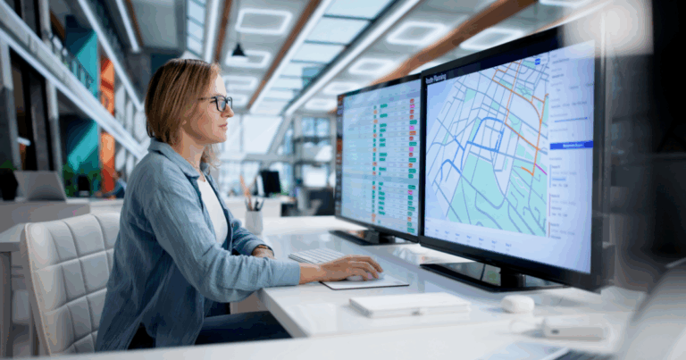 Profissional monitora mapas digitais e painéis de controle em múltiplas telas, analisando trajetos e dados logísticos em tempo real. A imagem representa a otimização de rotas.