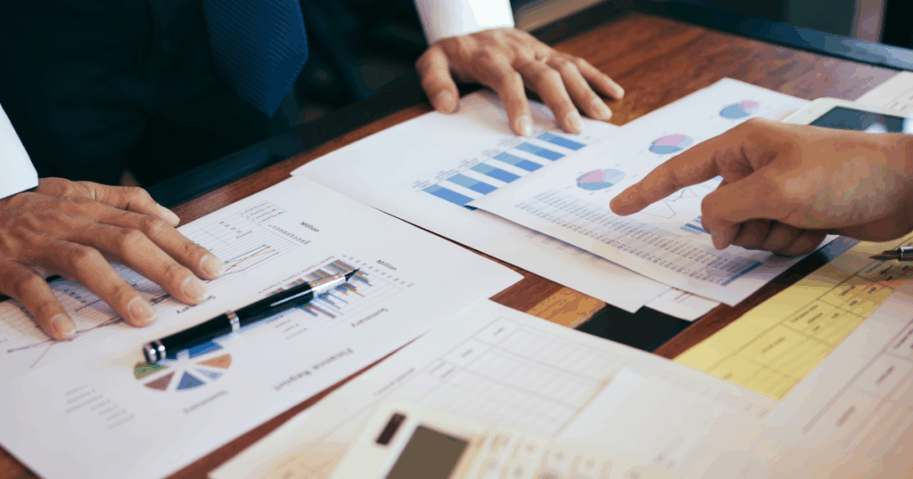 Profissionais analisando relatórios financeiros e gráficos durante uma reunião de gestão orçamentária para planejamento e controle de recursos da empresa.