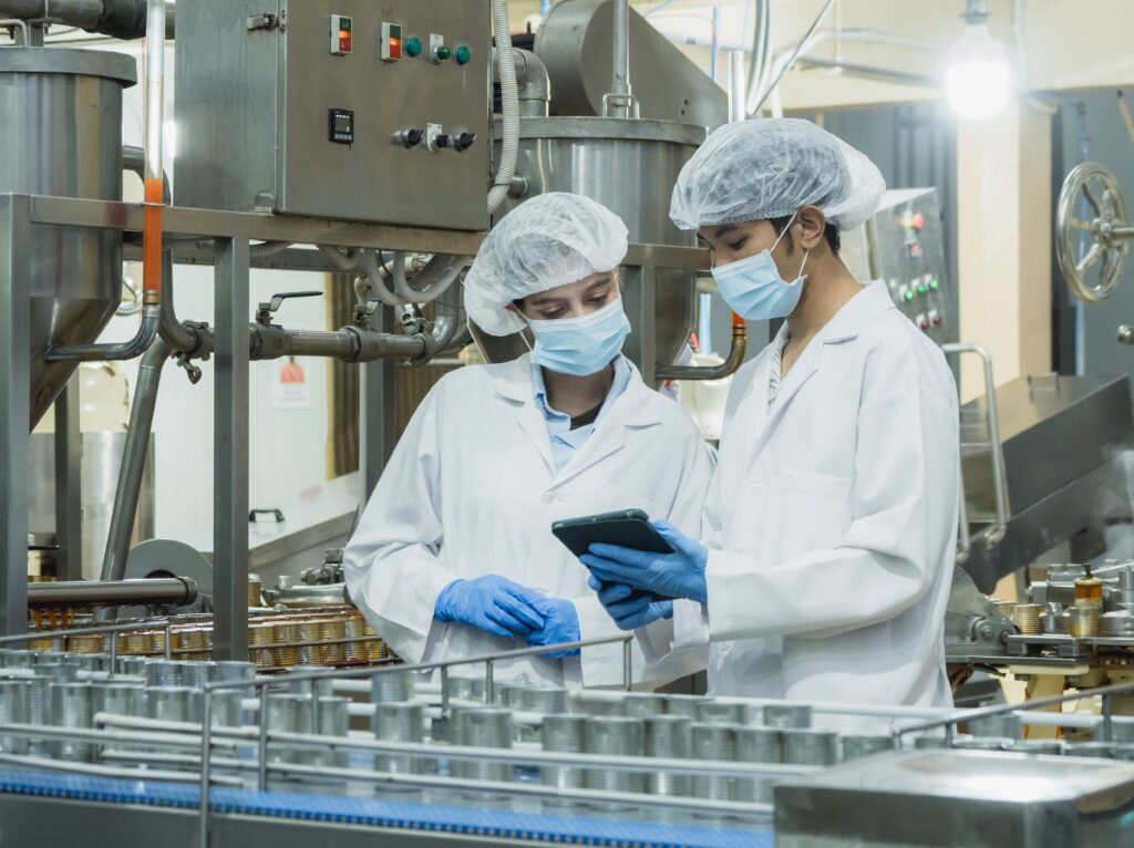 Profissionais inspecionam a linha de produção em uma indústria de alimentos, verificando processos e condições de higiene durante uma ação de vigilância sanitária de alimentos.
